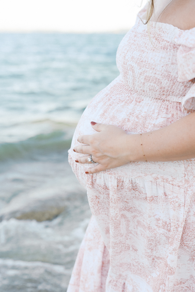 Close-up of a pregnant belly in a flowing pink dress at the shoreline of Folsom Lake, one of the best locations for family photos in Sacramento