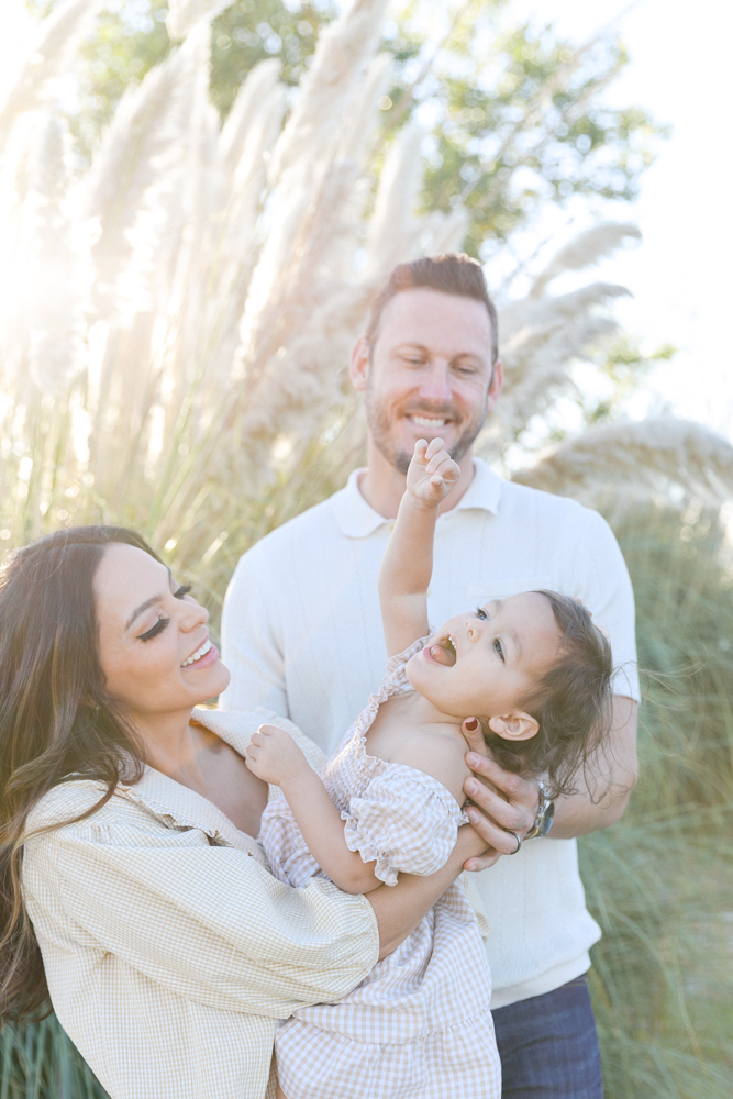 Dad laughing with toddler among tall pampas grass plumes in a Sacramento park
