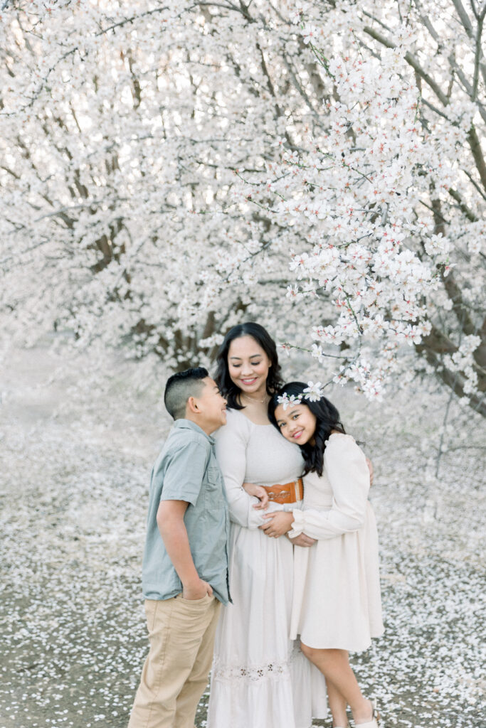 Family walking hand-in-hand under blooming almond blossom trees, one of the best locations for family photos in Sacramento in early spring