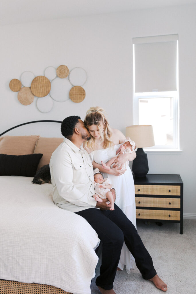 dad kissing mom's cheek while holding their twin baby girls
