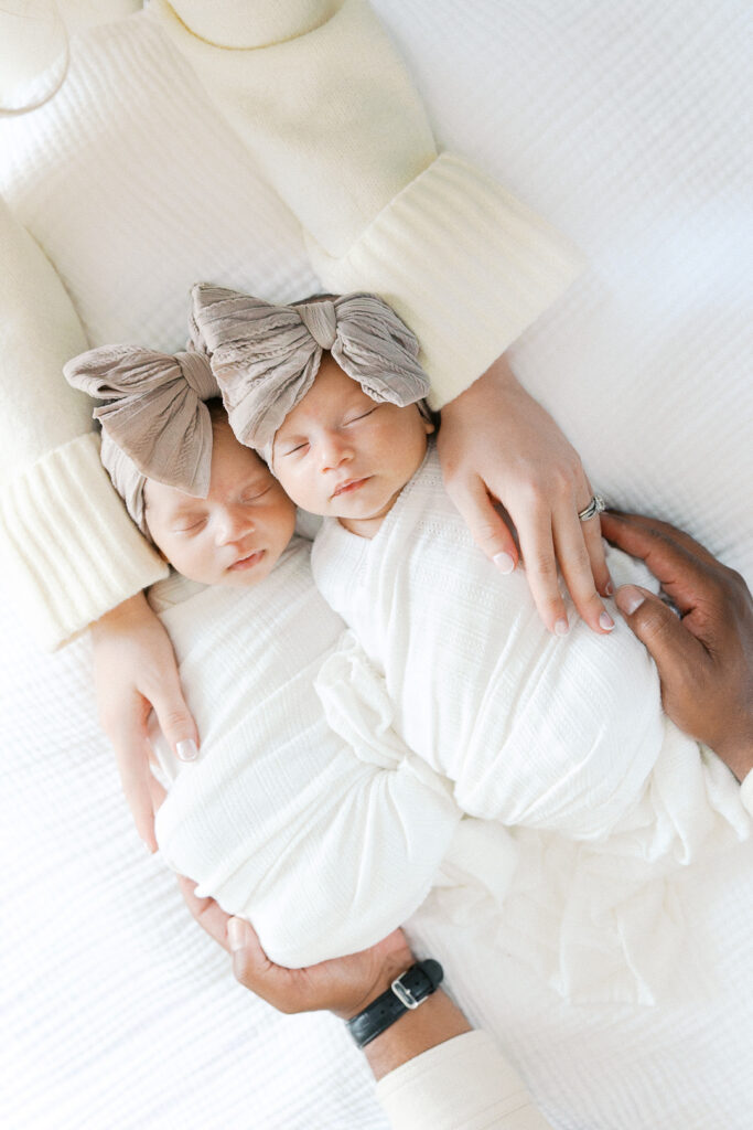 twin baby girls sleeping with mom and dad's hands on each side of them
