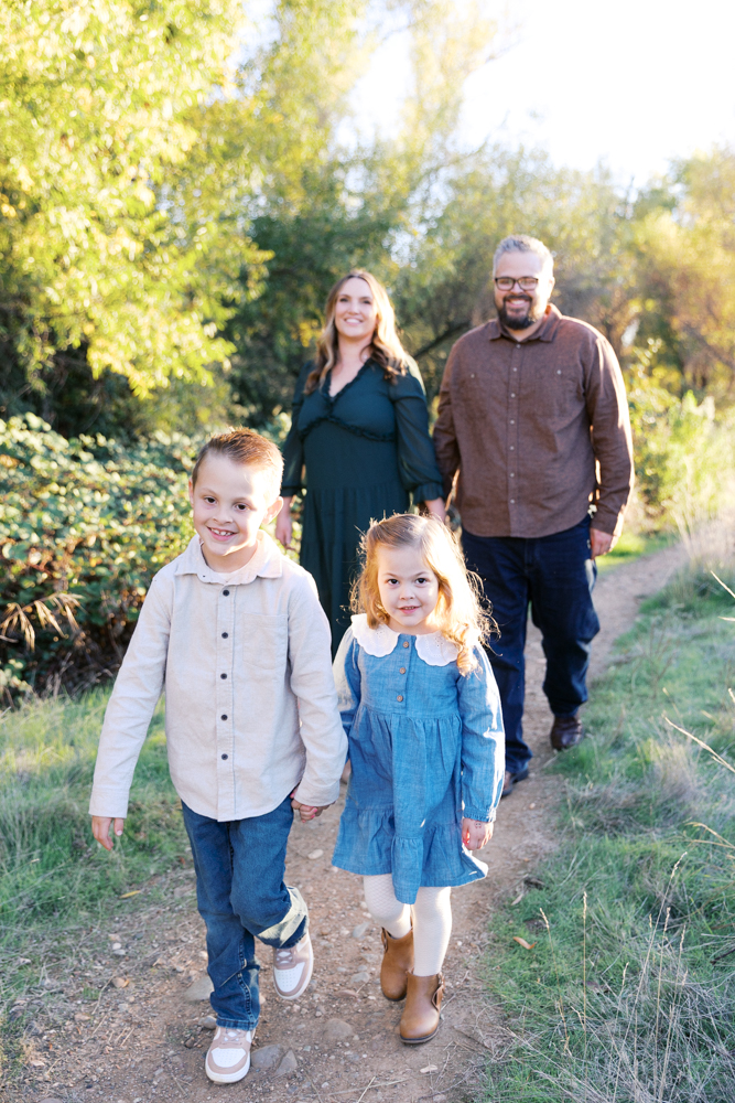 brother and sister walking down an outdoor path holding hands while mom and dad walk behind